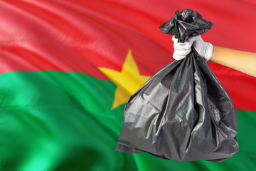 Burkina Faso environmental protection concept. The male hand holding a garbage bag on national flag background. Ecological and recycling theme with copy space.