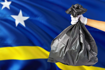 Curacao environmental protection concept. The male hand holding a garbage bag on national flag background. Ecological and recycling theme with copy space.