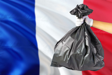 France environmental protection concept. The male hand holding a garbage bag on national flag background. Ecological and recycling theme with copy space.