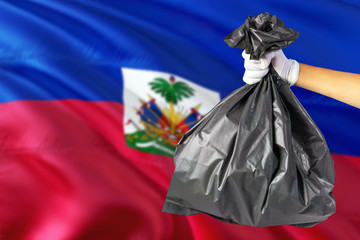 Haiti environmental protection concept. The male hand holding a garbage bag on national flag background. Ecological and recycling theme with copy space.