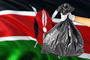 Kenya environmental protection concept. The male hand holding a garbage bag on national flag background. Ecological and recycling theme with copy space.