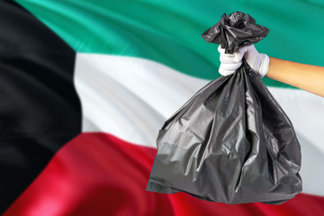 Kuwait environmental protection concept. The male hand holding a garbage bag on national flag background. Ecological and recycling theme with copy space.