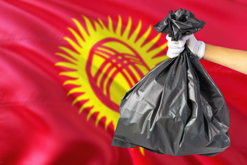 Kyrgyzstan environmental protection concept. The male hand holding a garbage bag on national flag background. Ecological and recycling theme with copy space.