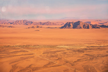 Fototapeta na wymiar Aerial view of the Namib Desert, showing long straight roads running through desolate terrain. Sossusvlei, Namibia.