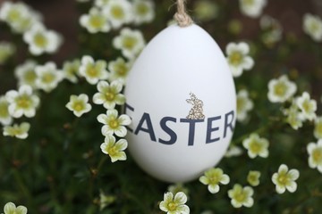 Easter time. White decorative egg with the inscription Easter  in white flowers on a blurred green spring garden background.Spring festive religious background.