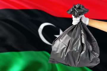 Libya environmental protection concept. The male hand holding a garbage bag on national flag background. Ecological and recycling theme with copy space.