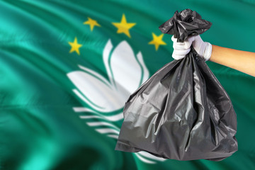 Macao environmental protection concept. The male hand holding a garbage bag on national flag background. Ecological and recycling theme with copy space.