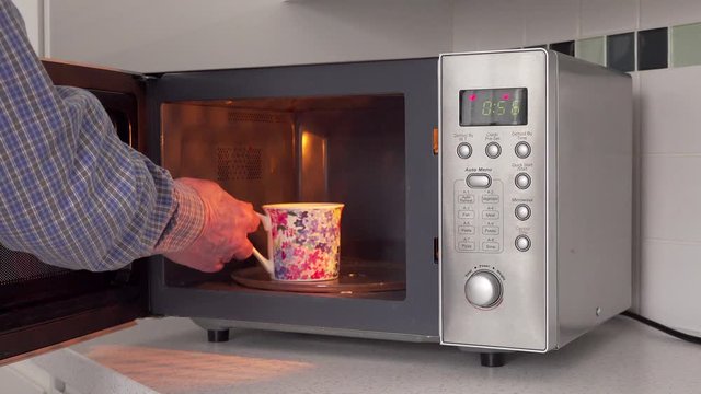 Operating microwave oven with mug in domestic kitchen