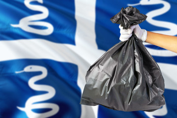 Fototapeta premium Martinique environmental protection concept. The male hand holding a garbage bag on national flag background. Ecological and recycling theme with copy space.