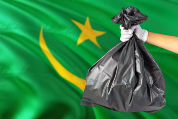Mauritania environmental protection concept. The male hand holding a garbage bag on national flag background. Ecological and recycling theme with copy space.