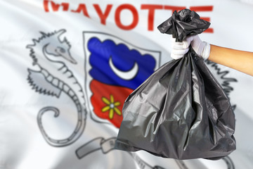 Mayotte environmental protection concept. The male hand holding a garbage bag on national flag background. Ecological and recycling theme with copy space.