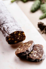 Sausage Cookie. Traditional chocolate sausage salami with cocoa, chocolate and pecans on white marble background decorated fir branches and cones. Holidays treat. Selective focus