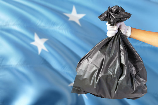 Micronesia Environmental Protection Concept. The Male Hand Holding A Garbage Bag On National Flag Background. Ecological And Recycling Theme With Copy Space.