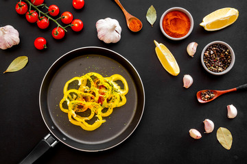 Cooking food concept. Pasta on frying pan near spices and vegetables on black background top-down