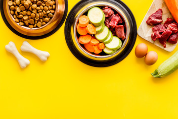 Dog feed - dry food and raw meat - near cheving bones on yellow background top view copy space