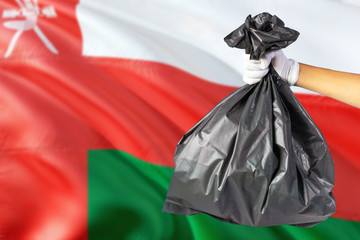 Oman environmental protection concept. The male hand holding a garbage bag on national flag background. Ecological and recycling theme with copy space.