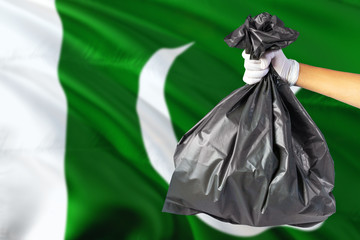 Pakistan environmental protection concept. The male hand holding a garbage bag on national flag background. Ecological and recycling theme with copy space.