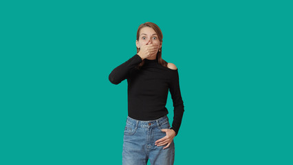 Fototapeta na wymiar A woman in blue jeans and a black turtleneck on a green background is surprised.