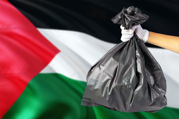 Palestine environmental protection concept. The male hand holding a garbage bag on national flag background. Ecological and recycling theme with copy space.
