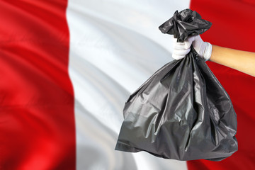 Peru environmental protection concept. The male hand holding a garbage bag on national flag background. Ecological and recycling theme with copy space.