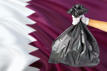 Qatar environmental protection concept. The male hand holding a garbage bag on national flag background. Ecological and recycling theme with copy space.