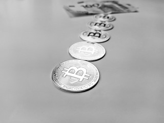 Bitcoin coins lined as earned cryptocurrency with paper money in the back showing that bitcoins are preferable way of banking