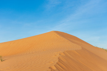 Fototapeta na wymiar Desert contrast of orange colored sand and bright blue sky in the rolling hills in Ras al Khaimah, in the United Arab Emirates.