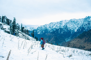 Woman walking on the snow carrying bag and tea kettel to serve tourist hot tea in winter tourist season with beautiful snow mountain landscape in the background, holiday destination, kashmir, India.