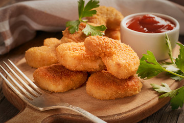 Close-up of chicken nuggets in a plate on a cutting board with chili tomato sauce and parsley on a wooden background
