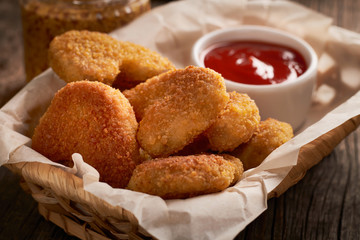 Close up of chicken nuggets in basket with parchment paper and chili tomato sauce on wooden background
