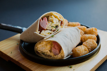 Breakfast burrito with sausage and scrambled egg and hash brown on a wooden plate