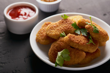 Close-up of chicken nuggets and tomato sauce and mustard seeds on a dark background
