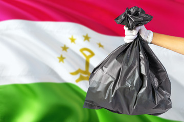 Tajikistan environmental protection concept. The male hand holding a garbage bag on national flag background. Ecological and recycling theme with copy space.