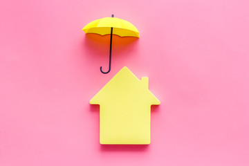 Property insurance concept. House cutout under umbrella on pink backgound top view copy space