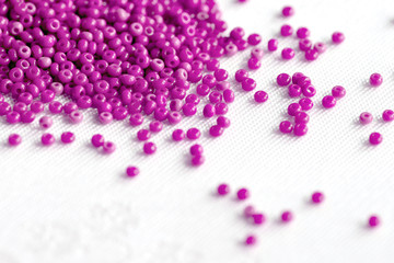Pink seed beads scattered on a textile surface close up. Handmade background