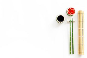 Table served for eating sushi. Chopsticks, bowls with ginger and sause, mat on white background top-down copy space