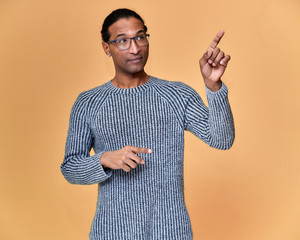 Portrait of a young African American man in glasses with a short haircut and with a white-toothed smile in a gray sweater on a pink background. Standing and talking right in front of the camera.