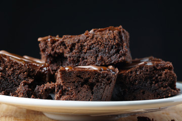 Close up of delicious dark fudgy brownies serve on round white plate ove wooden table.