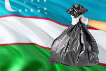 Uzbekistan environmental protection concept. The male hand holding a garbage bag on national flag background. Ecological and recycling theme with copy space.