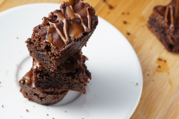 A stack of chocolate brownies serve on a round white plate. A piece of brownies placed on a wooden...