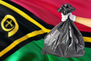 Vanuatu environmental protection concept. The male hand holding a garbage bag on national flag background. Ecological and recycling theme with copy space.