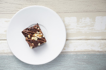 A moist dark chocolate brownie with mix nut on top served on white round plate over vintage background