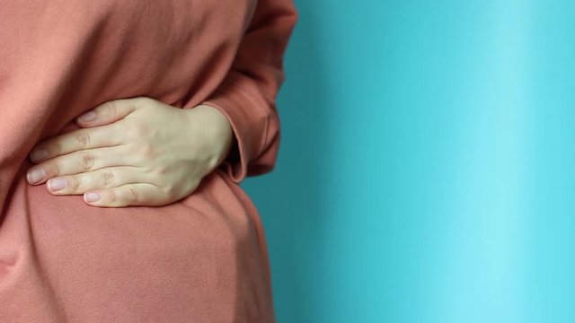 Girl holding her belly on a blue background, concept of acute pain, blue background