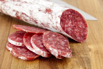 Close-up traditional sliced meat sausage salami on wooden board.