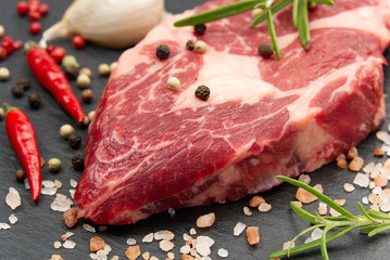 Raw rib eye steak with spices and vegetables. Ingredients for restaurant meal. Fresh meat, salt, rosemary, thyme, chilli, cherry tomatoes, garlic on black stone. Food background.