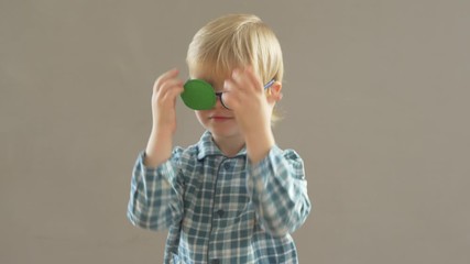 Portrait of funny child in new glasses with green spot to correct strabismus Orthopedic Boys Eye Patches nozzle for glasses for treatment of strabismus (lazy eye). Boy puts on and corrects glasses