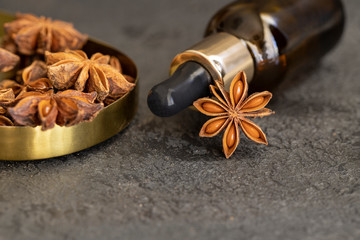 Essential anise stars oil  in glass bottle and natural anise star spice on a dark concrete background. Aromatherapy and Ayurveda concept.