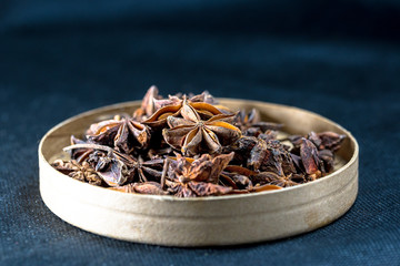 A small amount of anise and star anise is placed on a black background in a paper container.