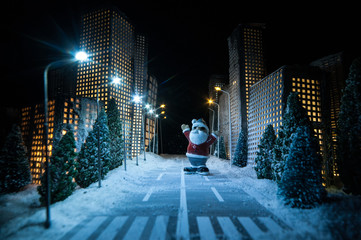 Little miniature city with road and lights. Decorative cute small houses in snow at night in winter. Creative Holiday concept. Christmas and New Year attributes decorated composition.