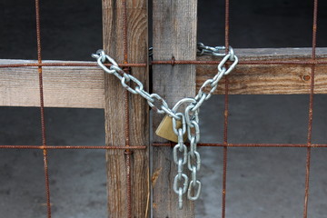 Closed improvised warehouse wooden doors with rusted metal net locked with padlock on strong chain...